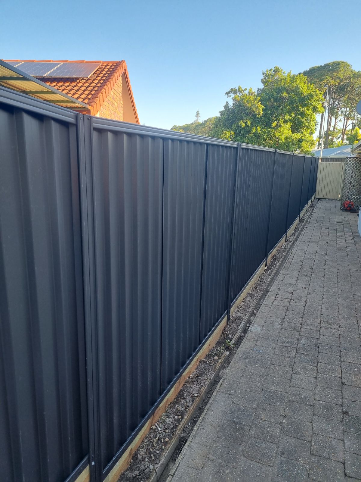 Long dark Colorbond fence beside a garden